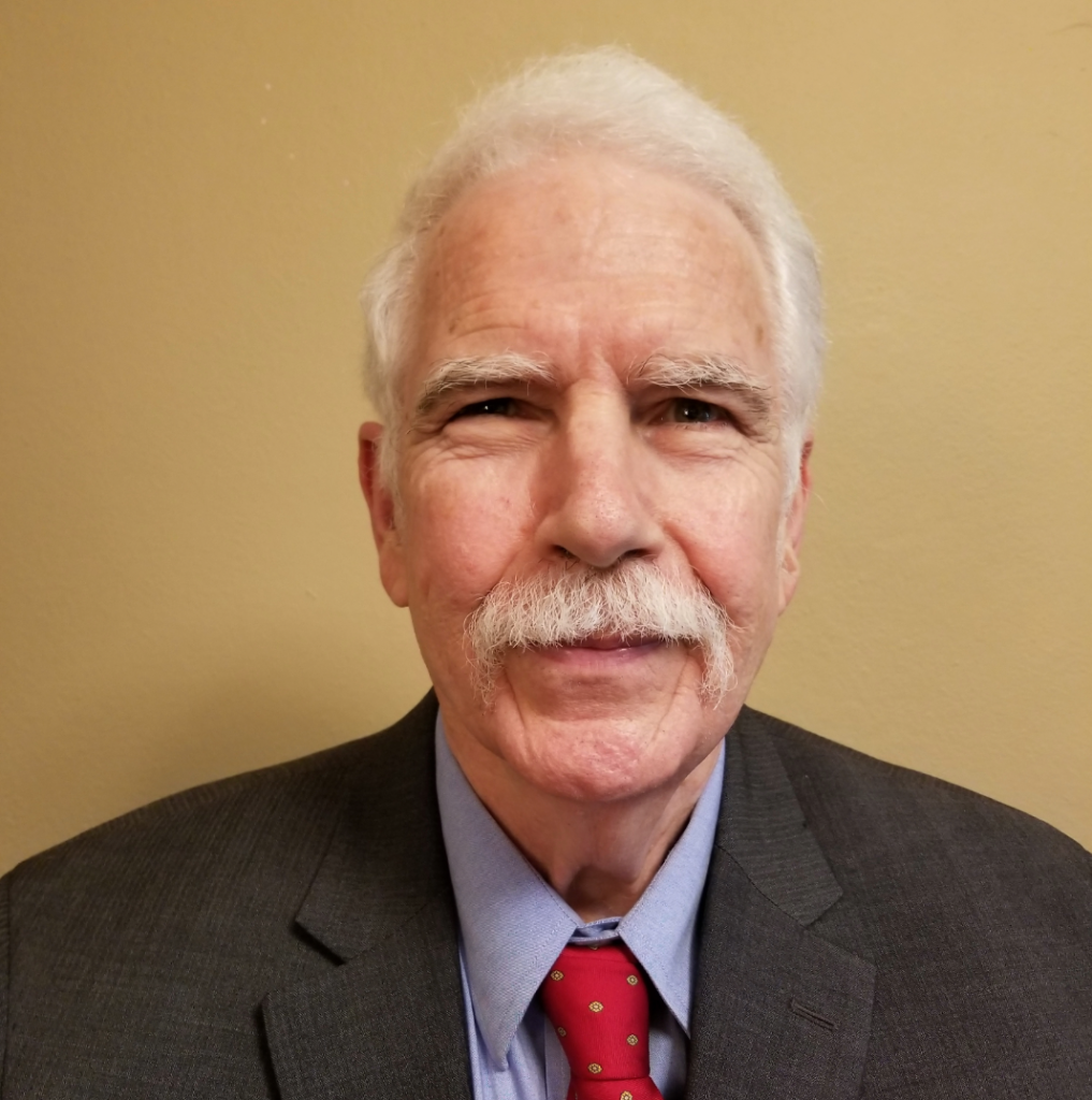 Man with grey hair and mustache looks at camera