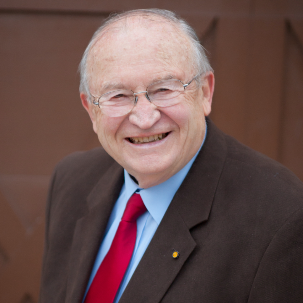 Man in suit with grey hair and glasses smiles at camera